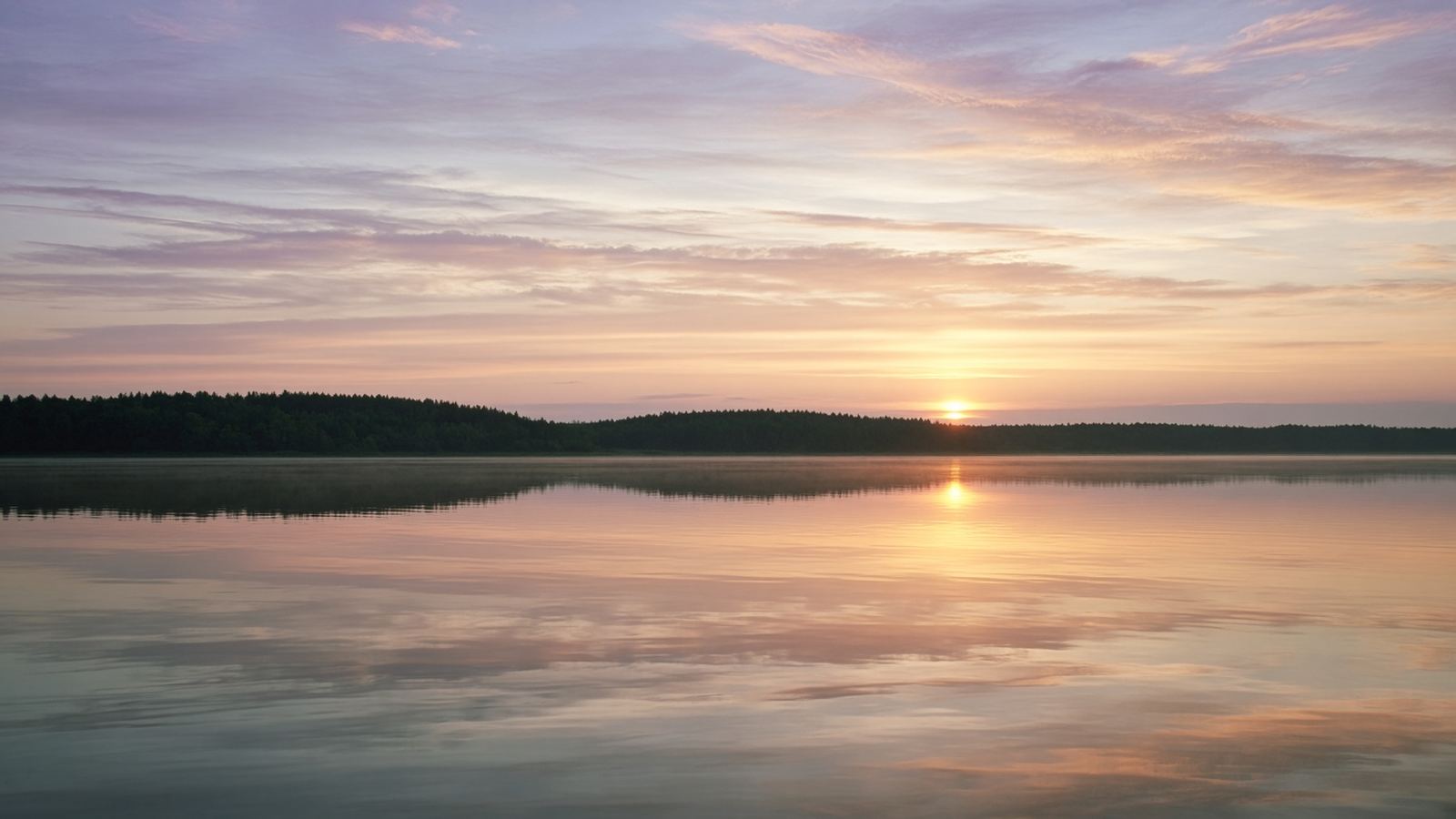 A still lake at sunrise, peach and lilac sky over quiet water